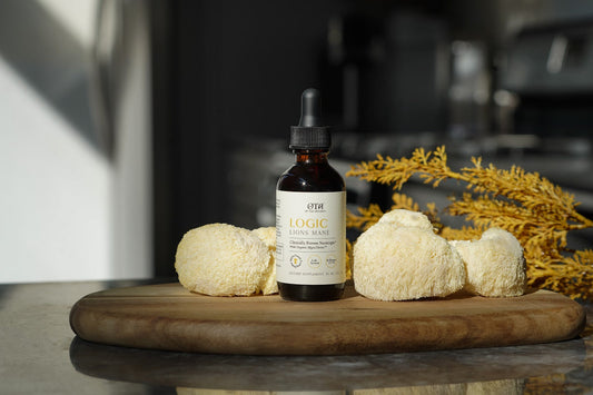 A bottle of Logic Lion's Mane tincture on a wooden board beside whole lion's mane mushrooms