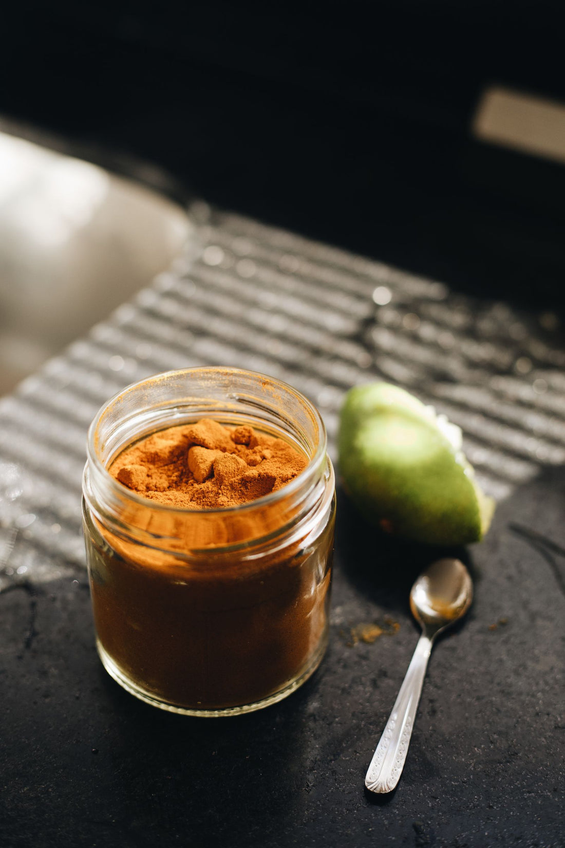 A jar of golden turmeric paste beside fresh lime on a woven mat