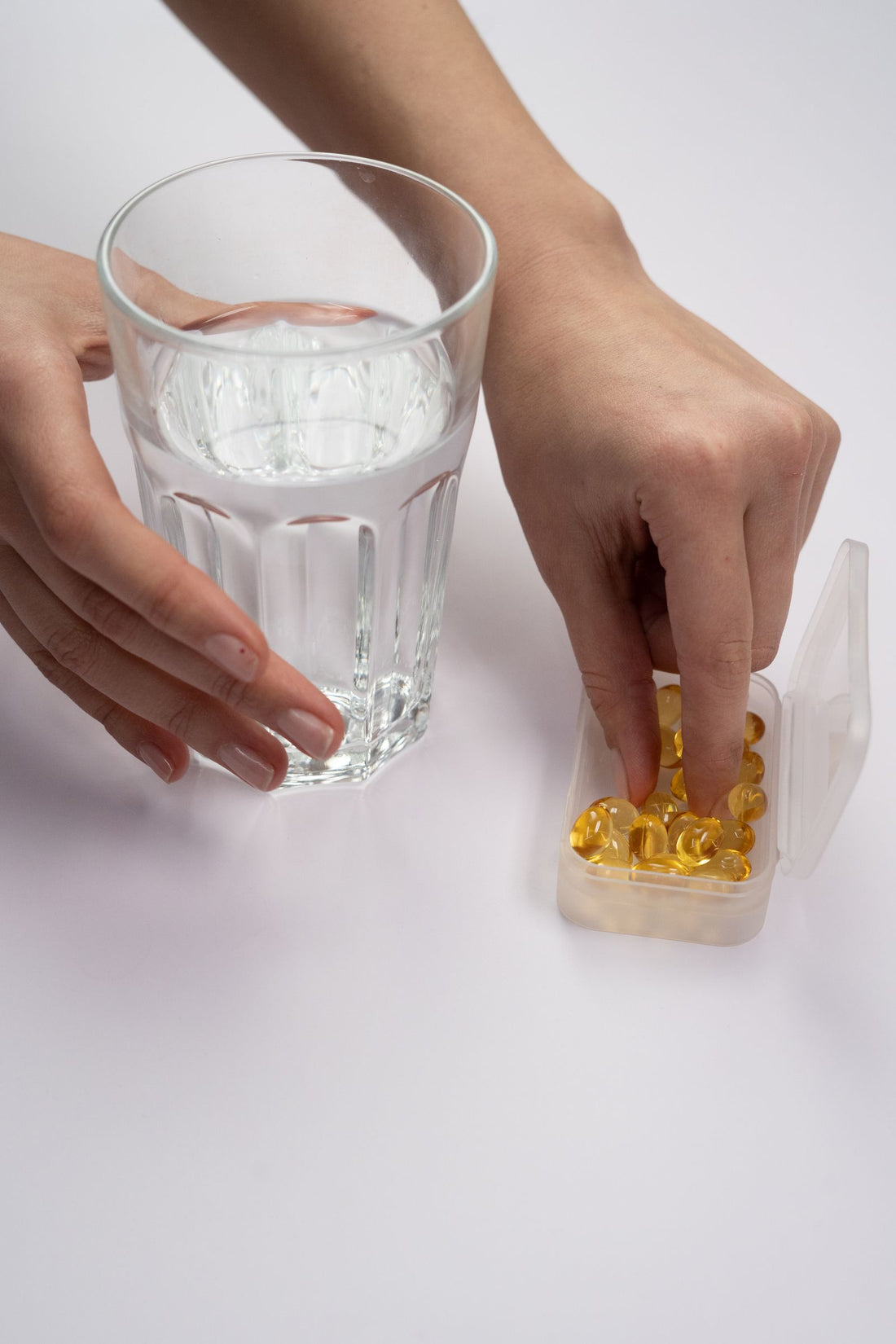 A hand holding supplements beside a glass of water on a kitchen counter