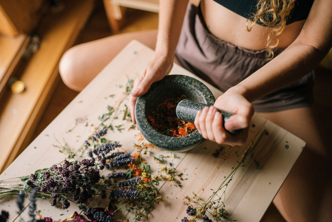 Hands sorting loose dried herbs on a wooden work surface