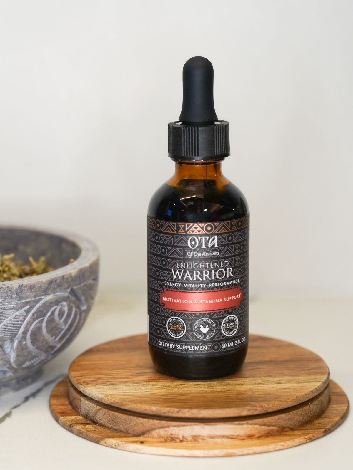 Enlightened Warrior liquid tincture supplement bottle standing on a wooden platform next to a pestle containing herbs.